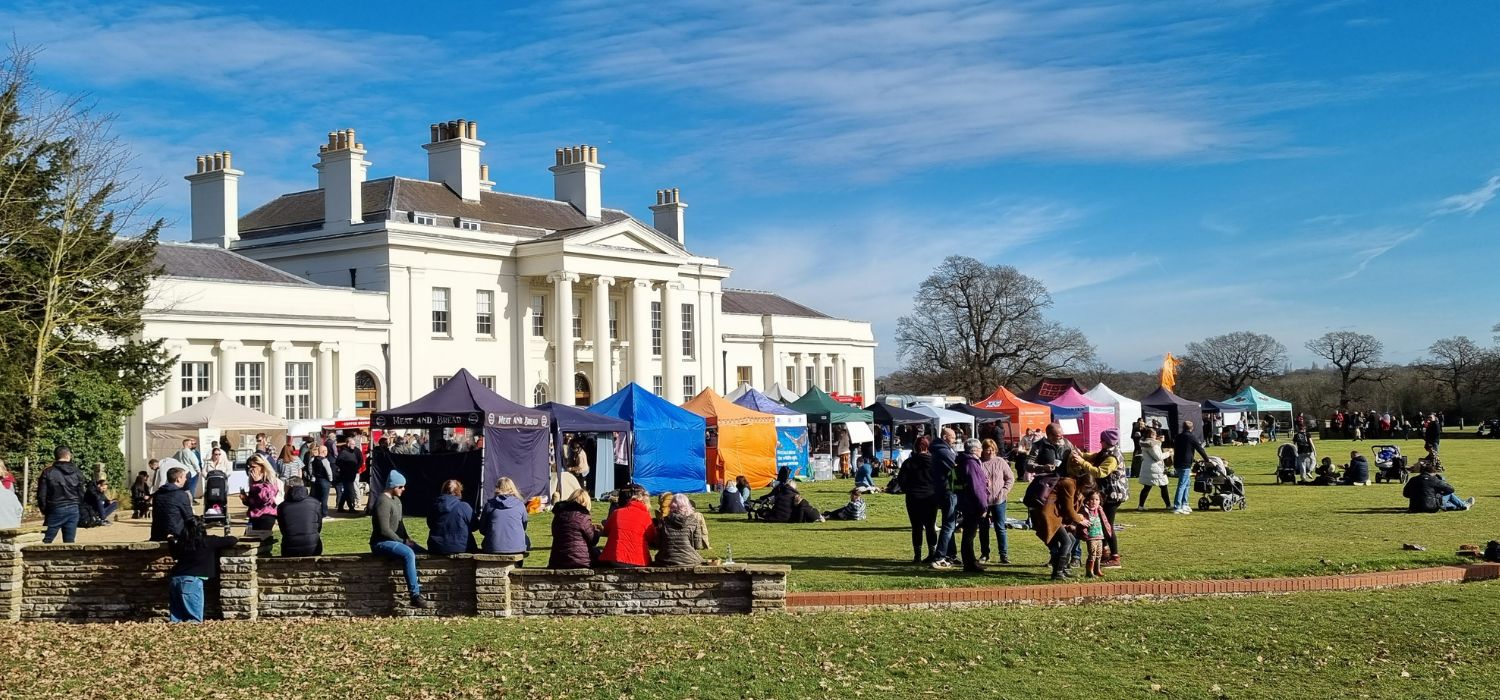A food festival is happening outside Hylands House. Crowds of people are amongst the various stands.