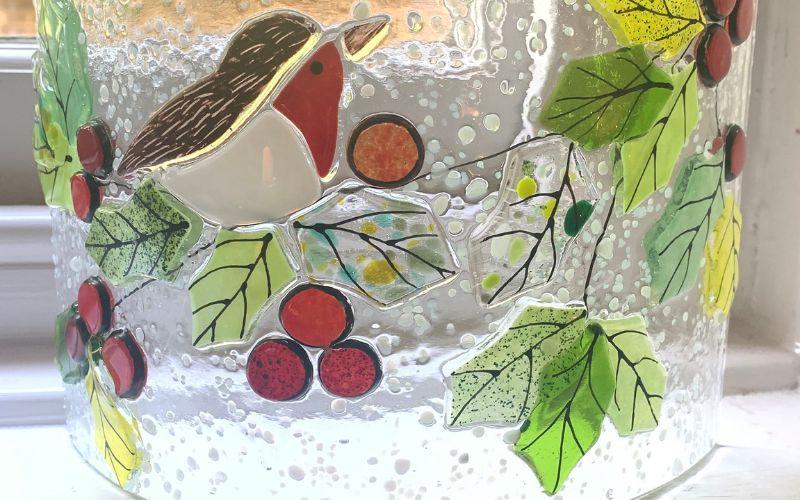 A warm glass decoration featuring a robin sitting on holly.