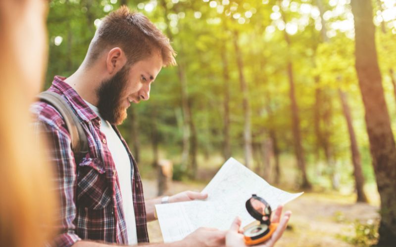 A man holding a map in the woods while someone next to him holds up a compass.