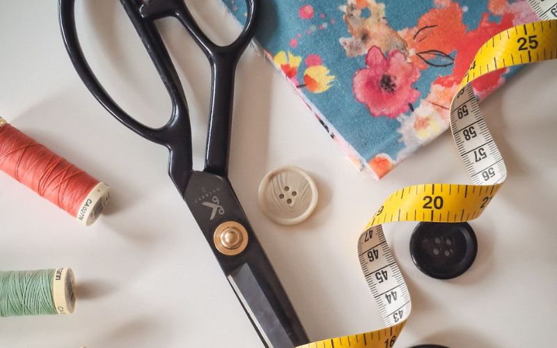 Scissors, thread and measuring tape laying on a table.